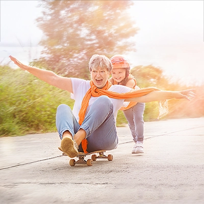 Lachende Frau auf Skateboard wird von Kind angeschoben